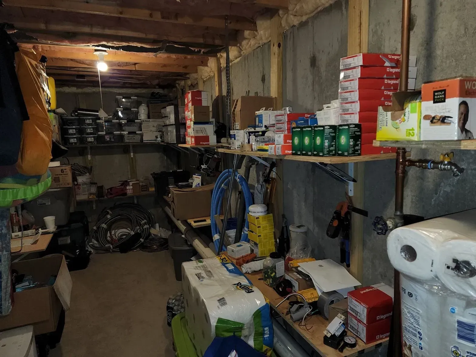 Cluttered basement storage area with shelves, boxes, tools, and household supplies under exposed beams