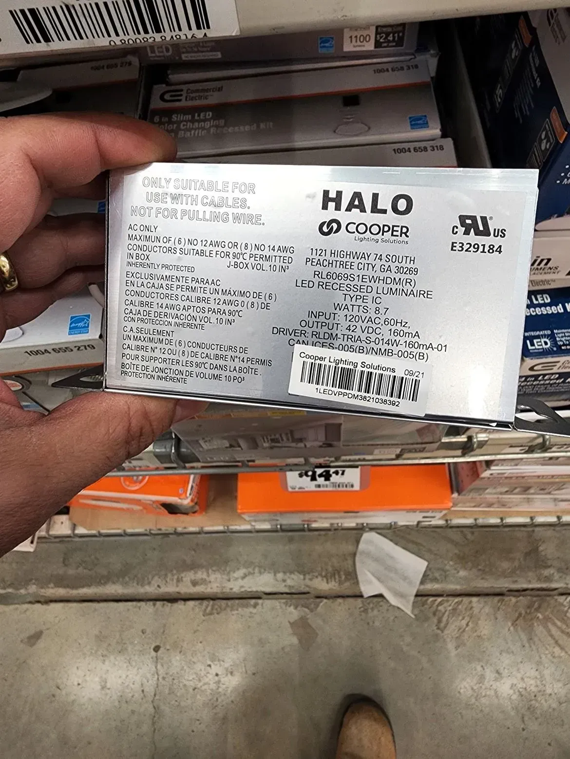 Hand holding a white HALO Coffee box in front of a shelf of stocked products.