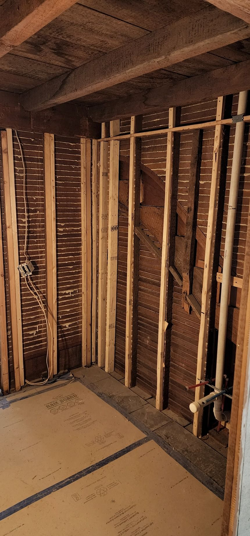 Unfinished room framing with exposed wooden studs, joists, and subfloor under construction.