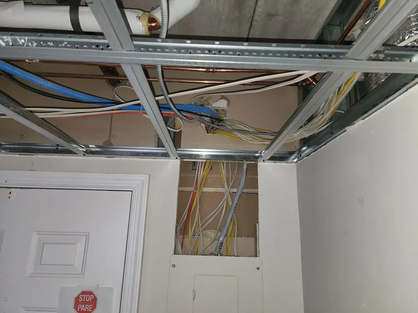 Exposed ceiling framing and wiring above a white door in an unfinished room