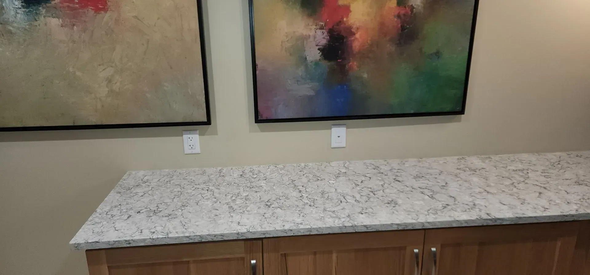 Kitchen counter with speckled granite top and wooden cabinets beneath, against a wall with abstract artwork.