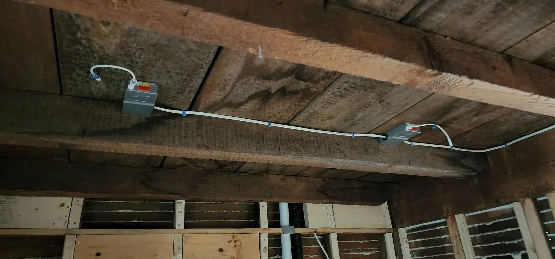 Exposed wooden ceiling with wiring and two hanging light fixtures in an unfinished room