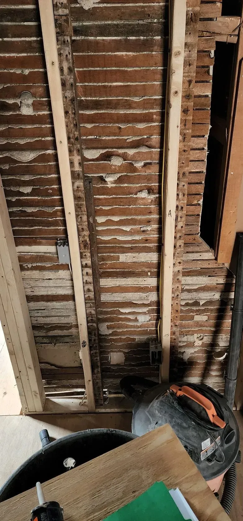 Exposed wooden ceiling joists with a ladder and tools below, showing a room under renovation