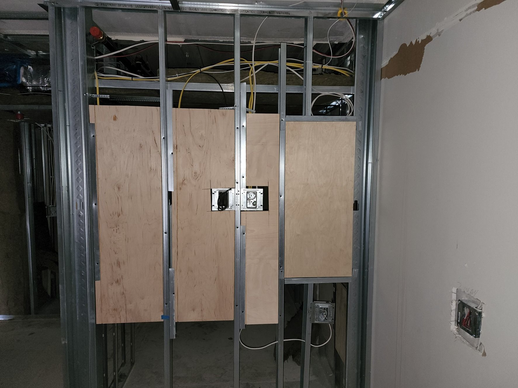 Exposed interior wall framing with drywall panels and electrical boxes in an unfinished room