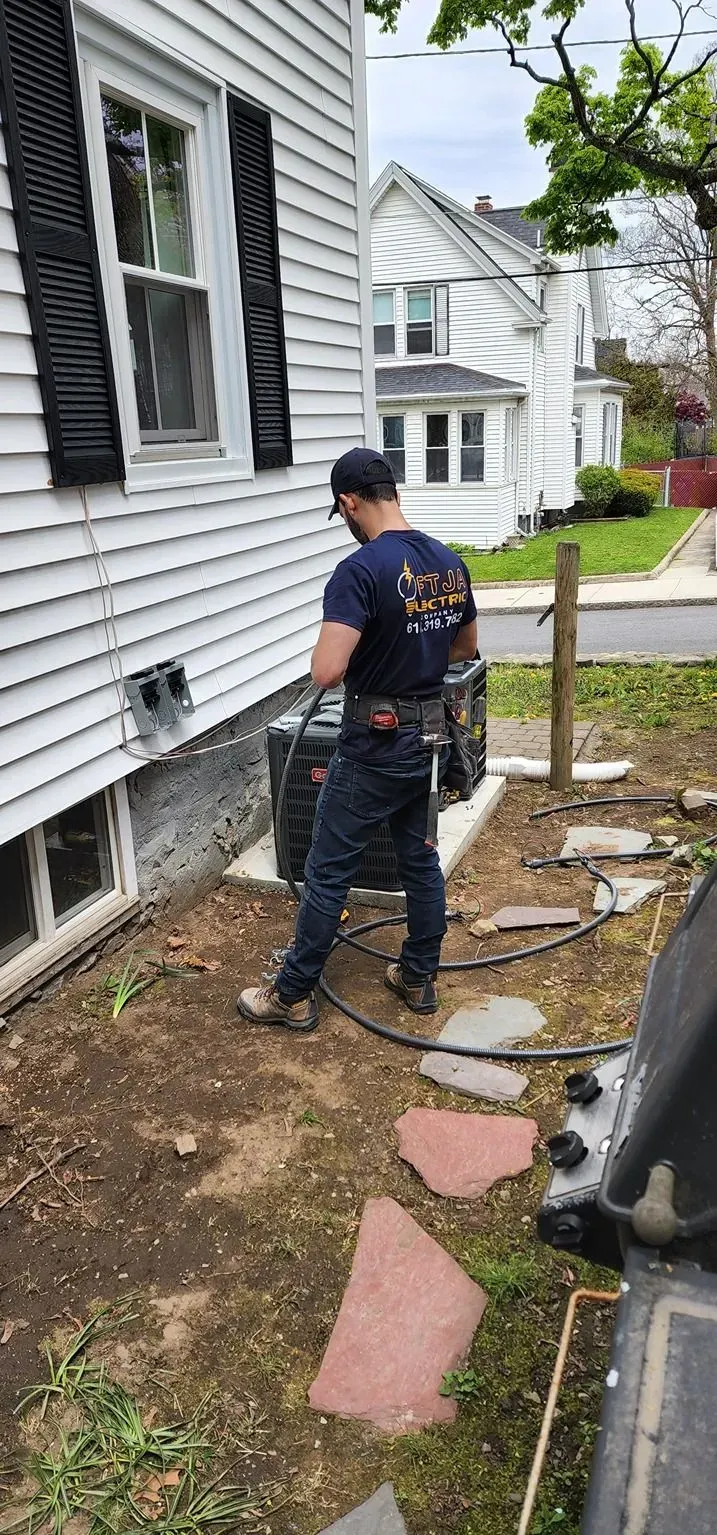 Worker inspecting a house foundation beside white siding, black shutters, and a garden hose.