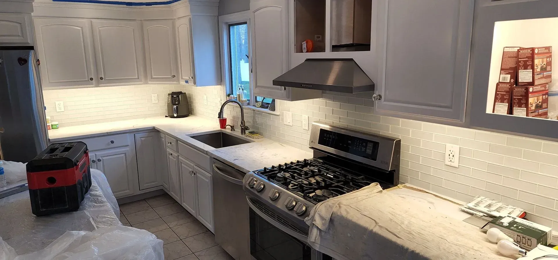 Bright kitchen with gray cabinets, white countertops, stainless stove, and a small red bucket on the counter.