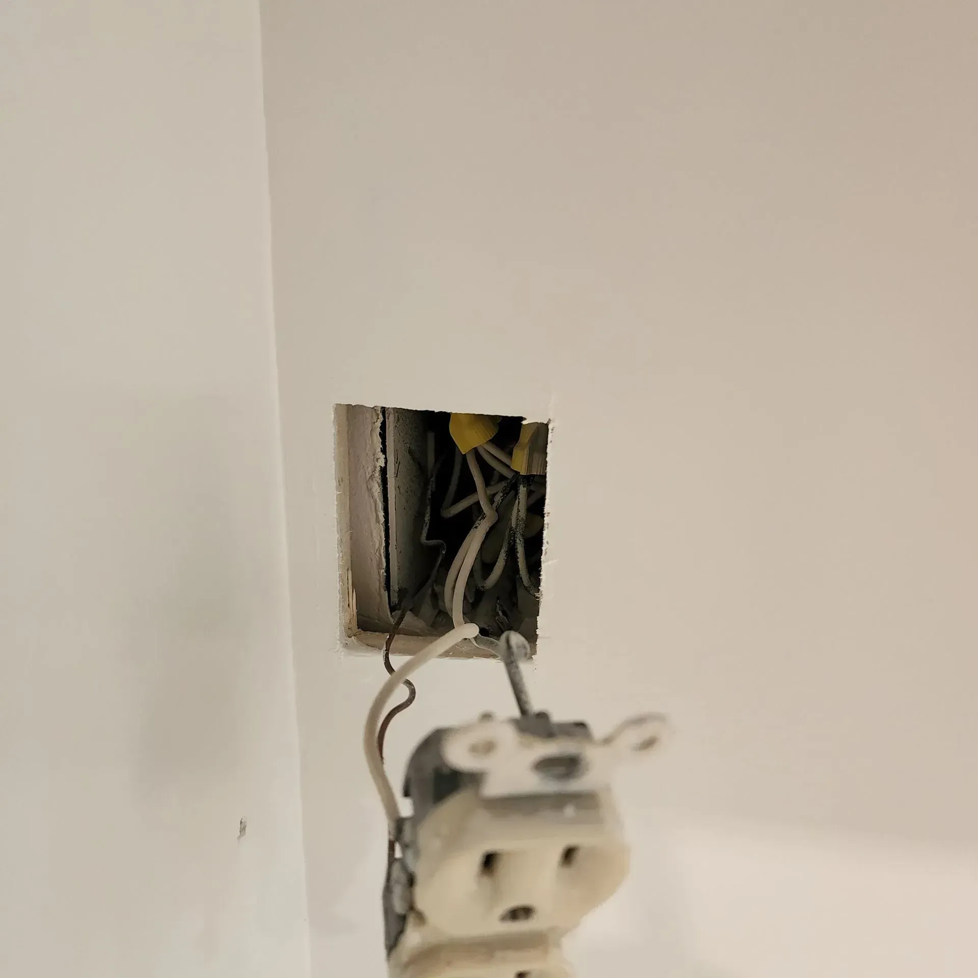 Open electrical wall outlet box with exposed wires and a loose outlet hanging out