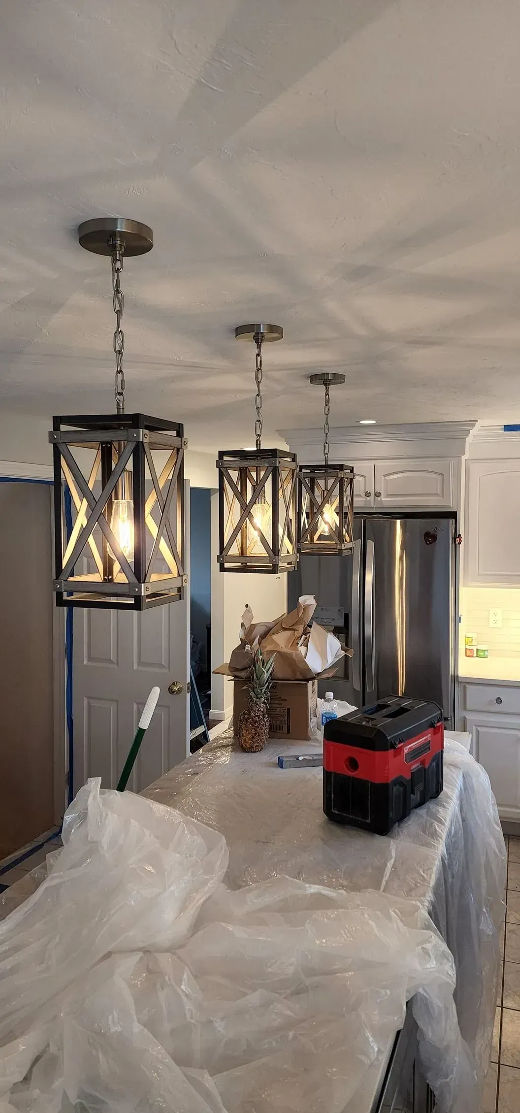 Hallway with hanging pendant lights and furniture wrapped in plastic, suggesting home renovation.