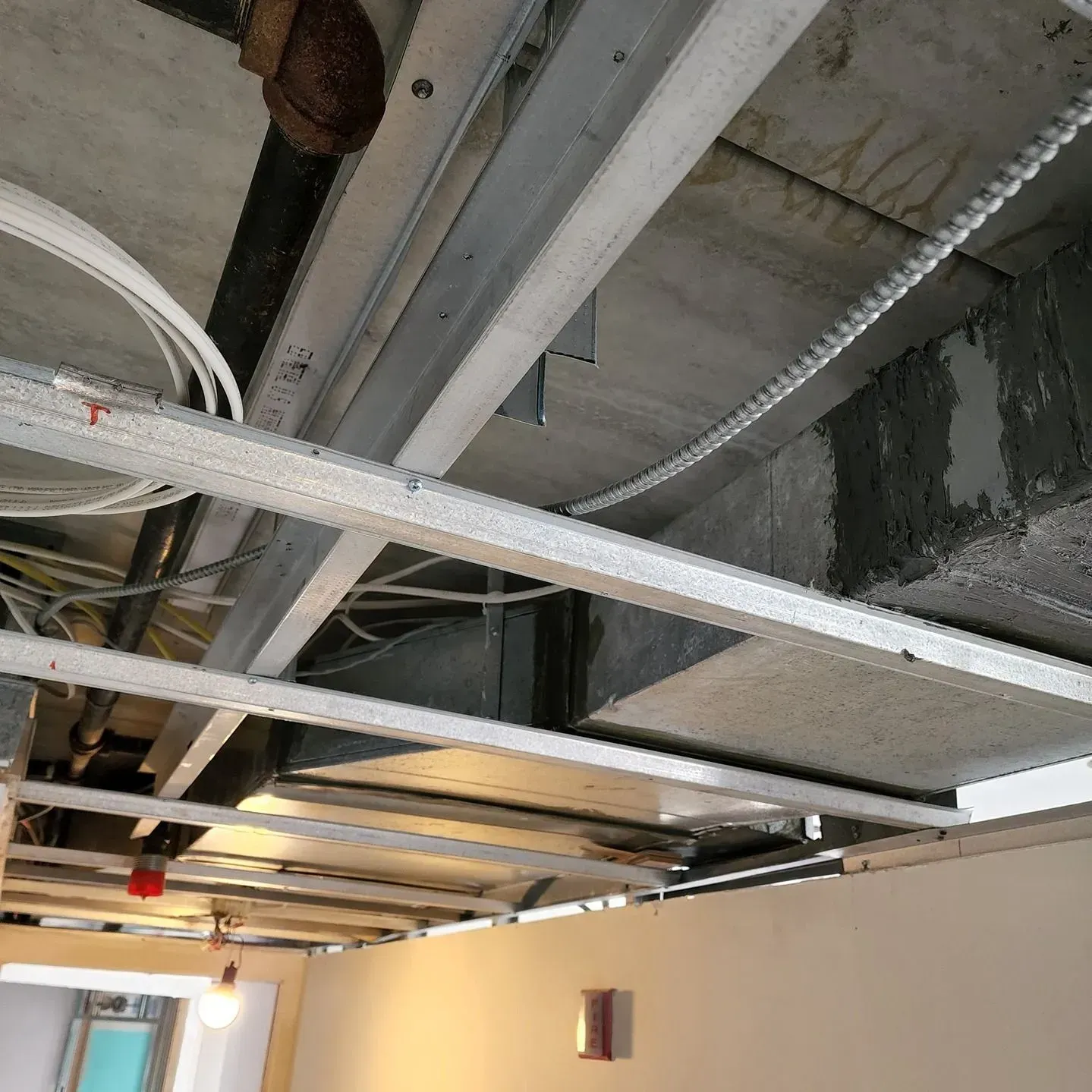 Exposed ceiling beams and ductwork in an unfinished interior room with white walls.