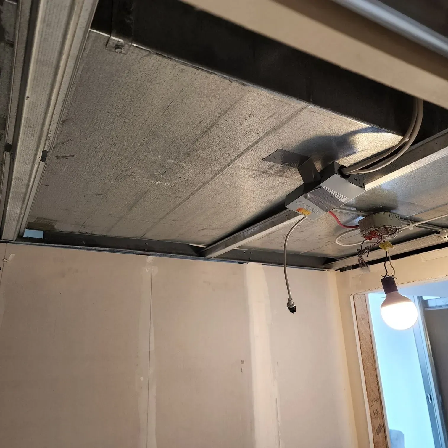 Ceiling with exposed insulation, hanging wires, and a bare light bulb in a room under construction