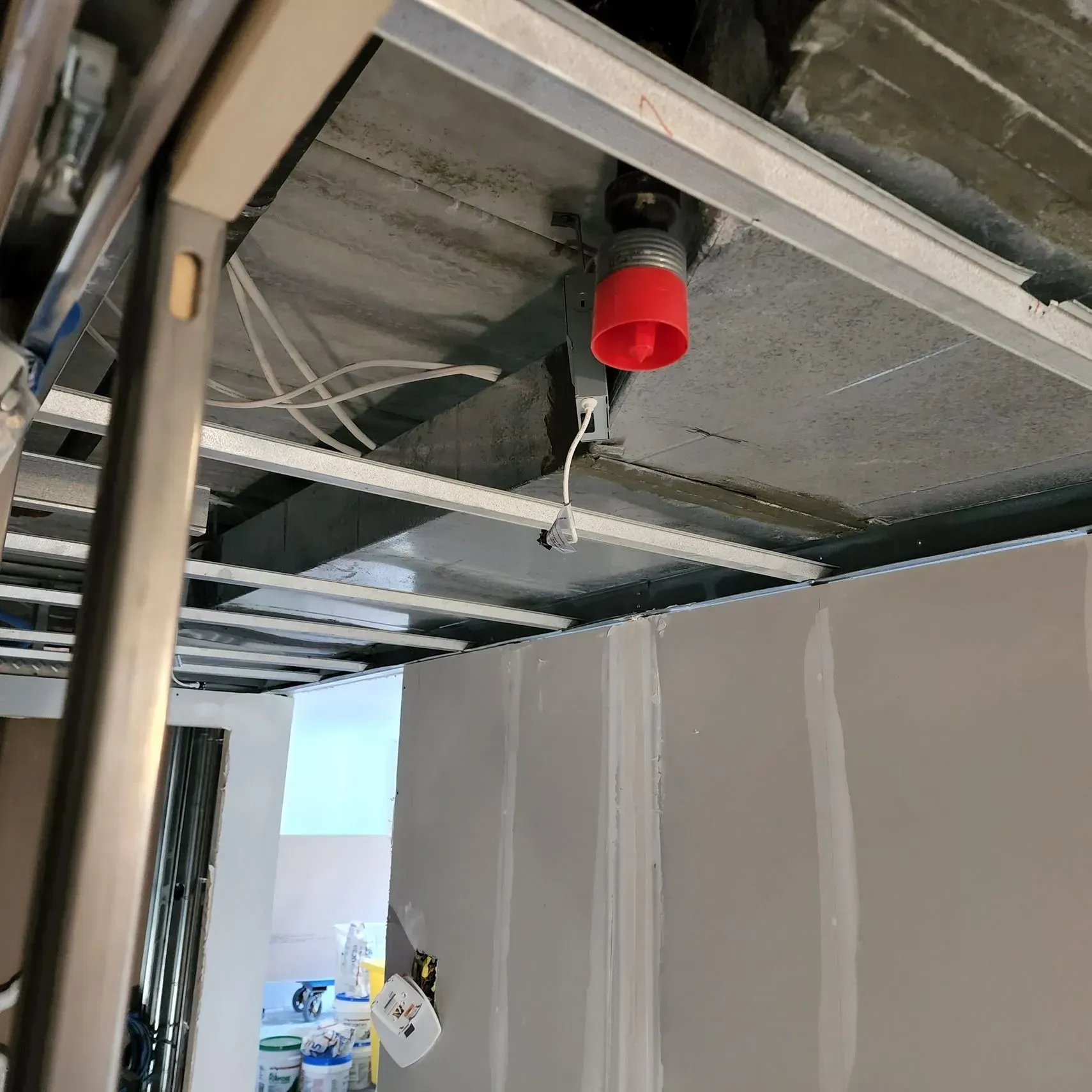 Ceiling under construction with exposed beams, wiring, and a red fire sprinkler head.