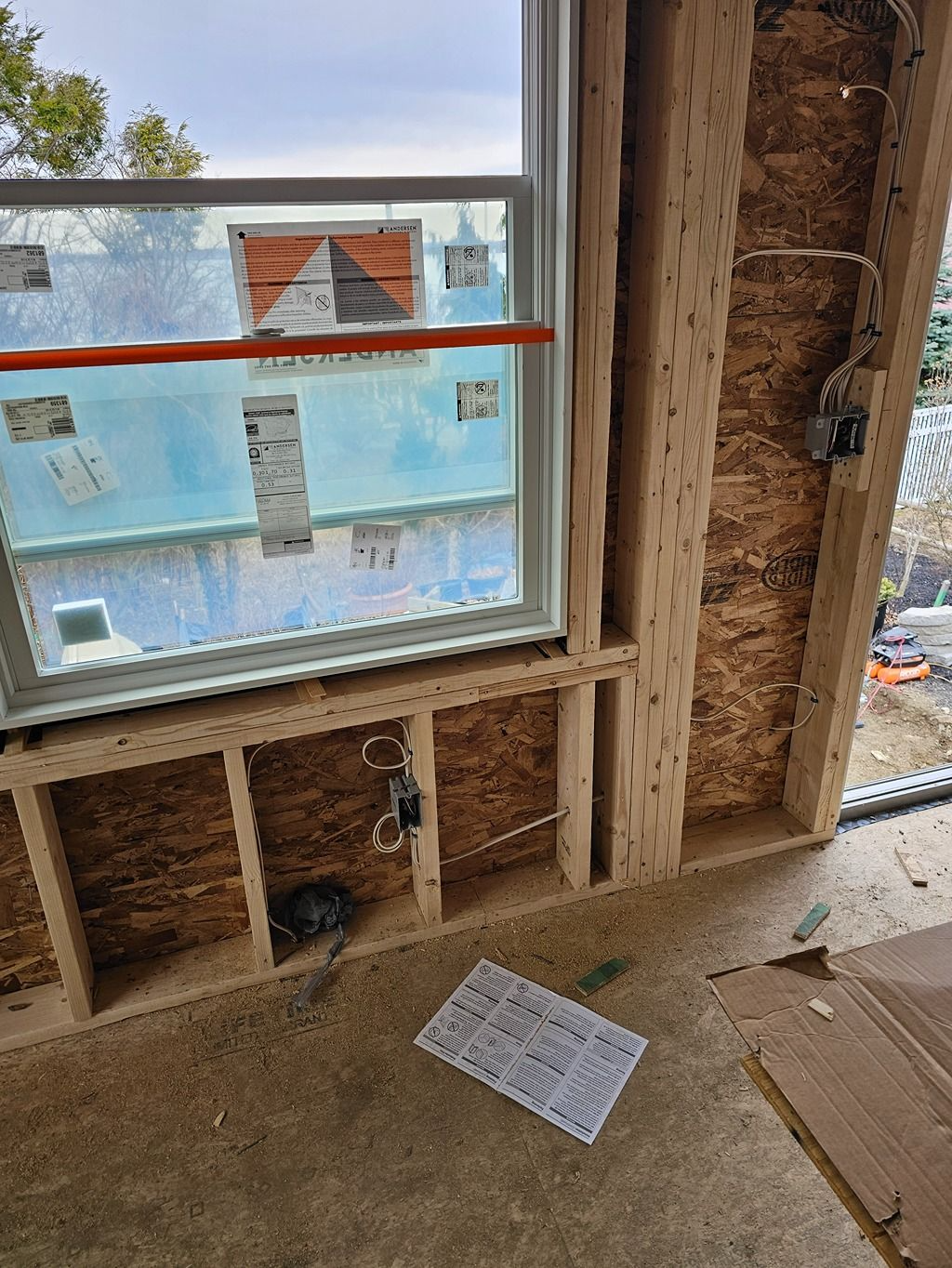 Interior construction framing with a window overlooking a blue building outside.
