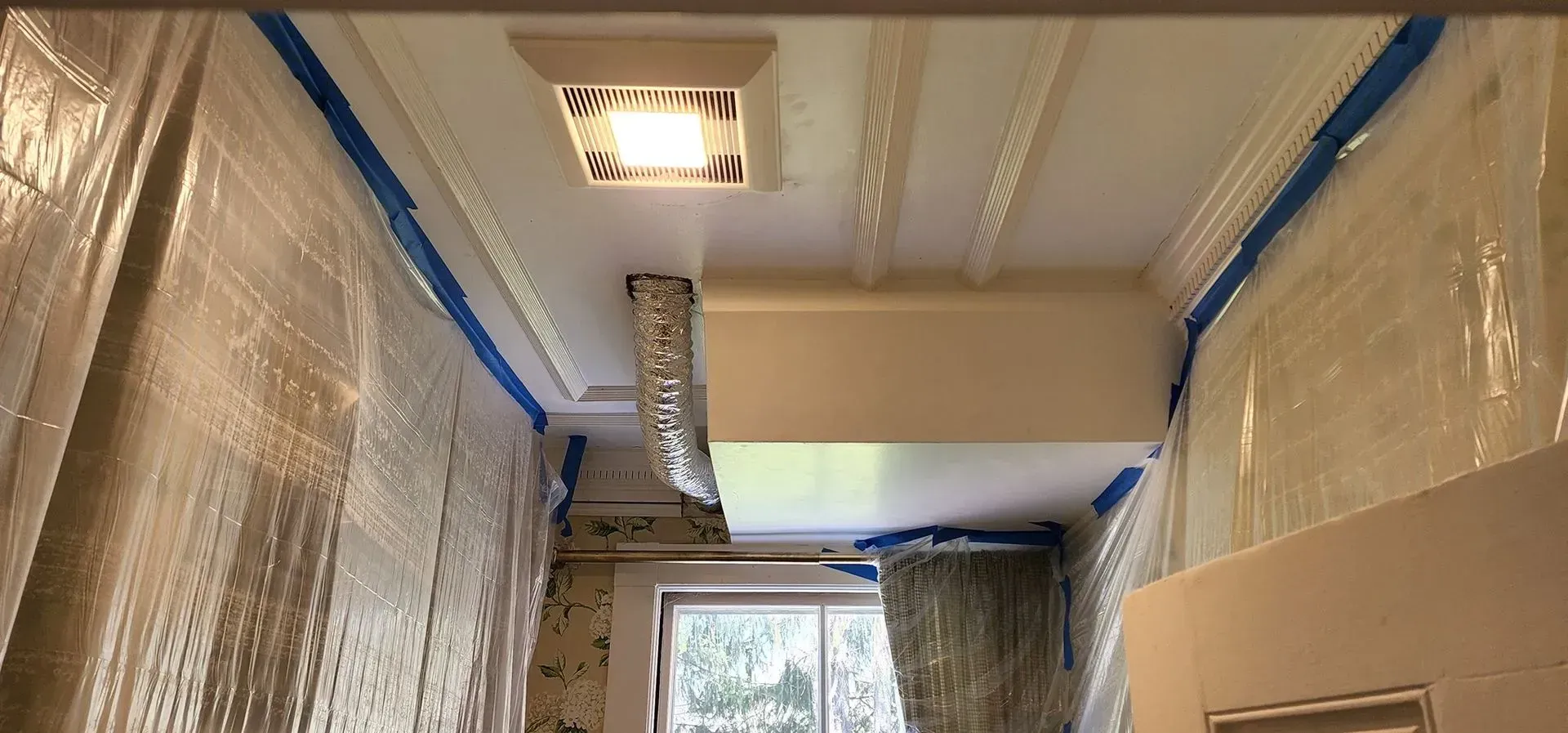 Plastic-covered hallway under renovation with exposed ductwork and a window at the end