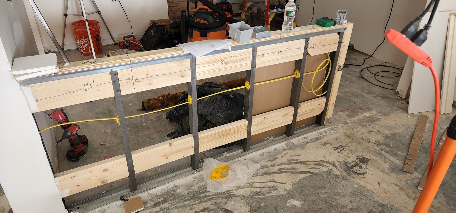 Construction site with a long wooden workbench, tools, and exposed framing against a concrete floor.