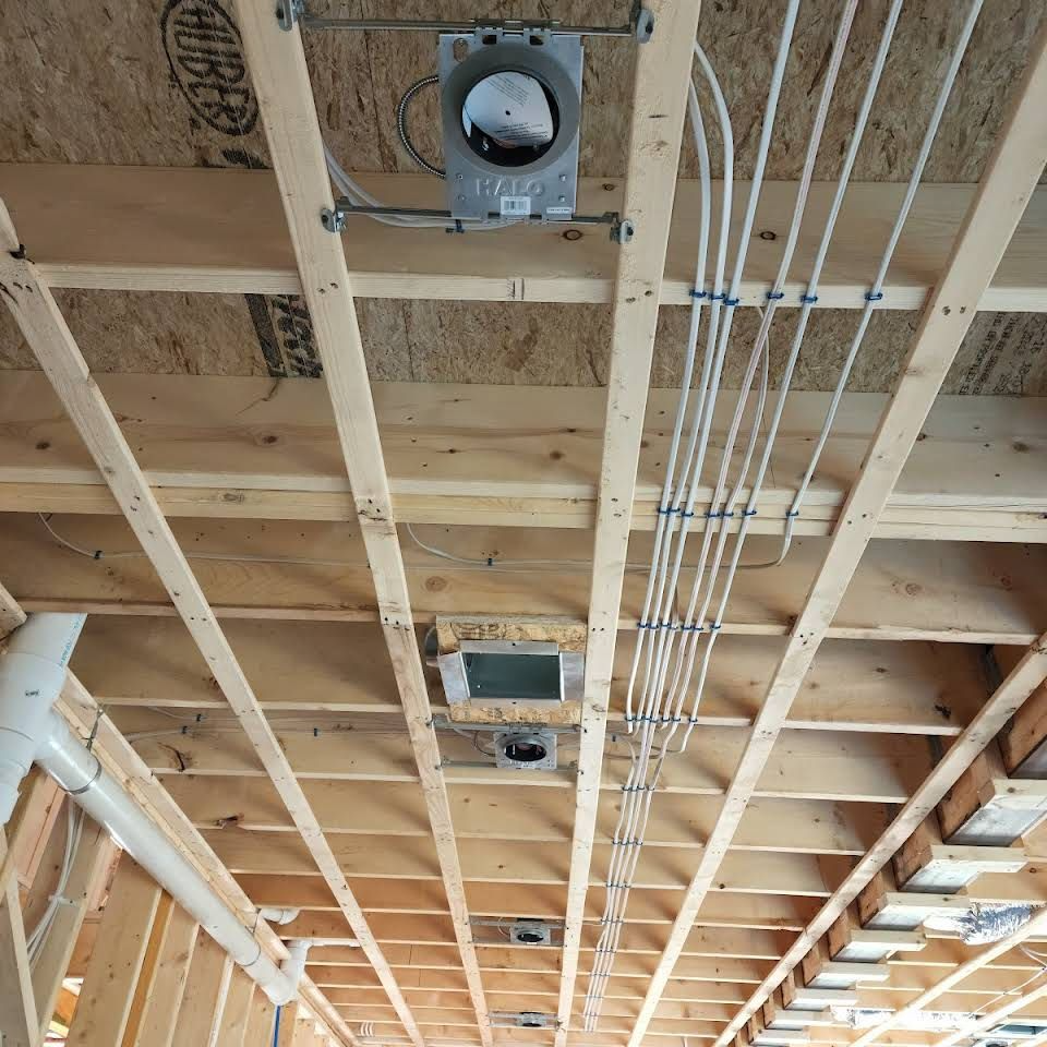 Exposed ceiling framing with electrical wiring and two recessed light fixtures in an unfinished room