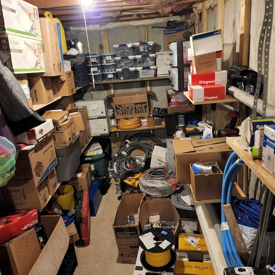 Cluttered storage room packed with boxes, tools, and miscellaneous household items on shelves and floor