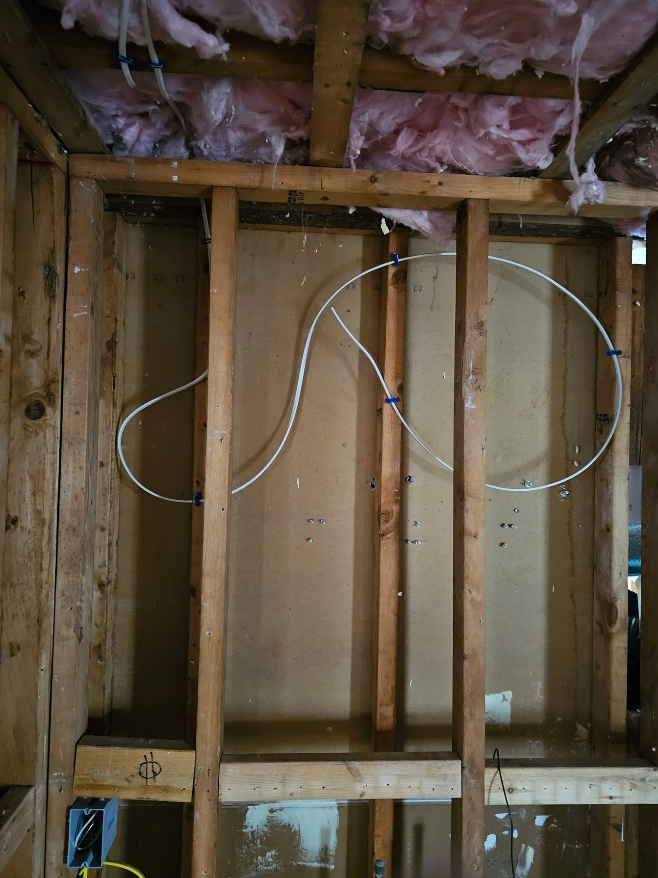 Exposed wall framing with electrical wiring and pink insulation in an unfinished room