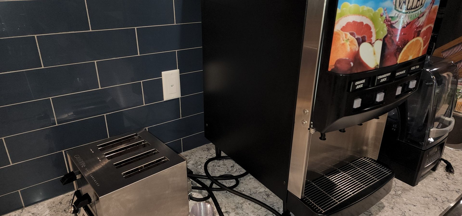 Kitchen counter with a black coffee machine, cup dispenser, and tiled backsplash beside a colorful wall art panel