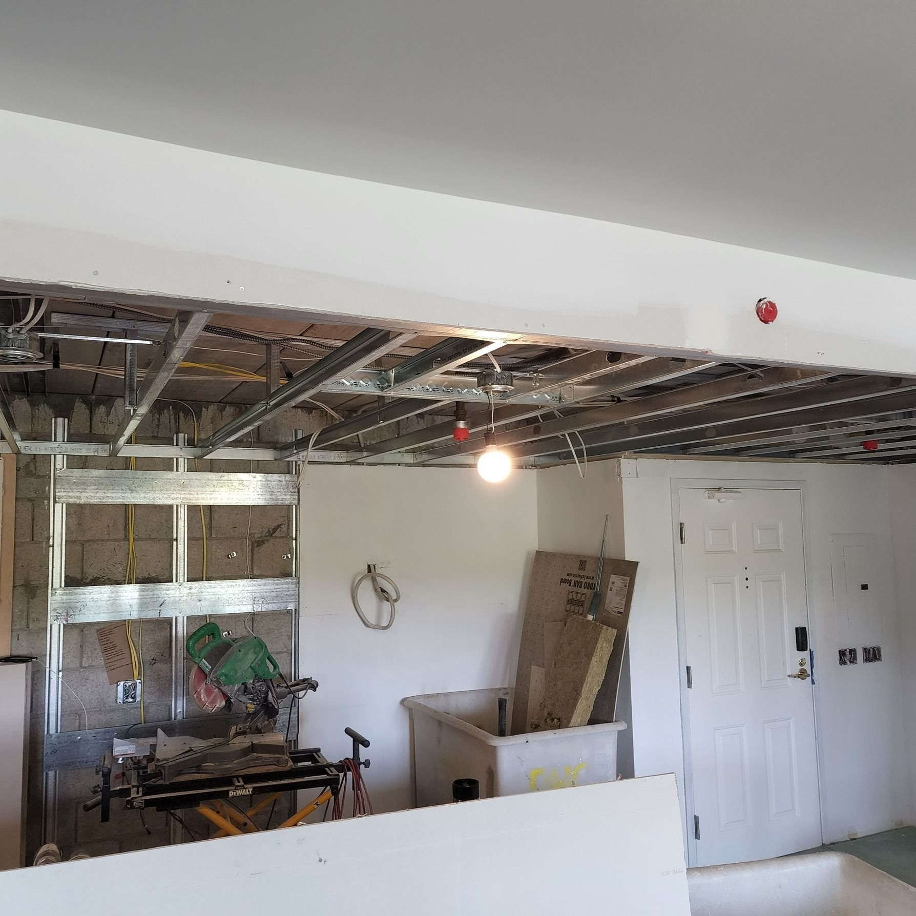 Partially renovated room with exposed ceiling beams, a hanging light, and doors on the right