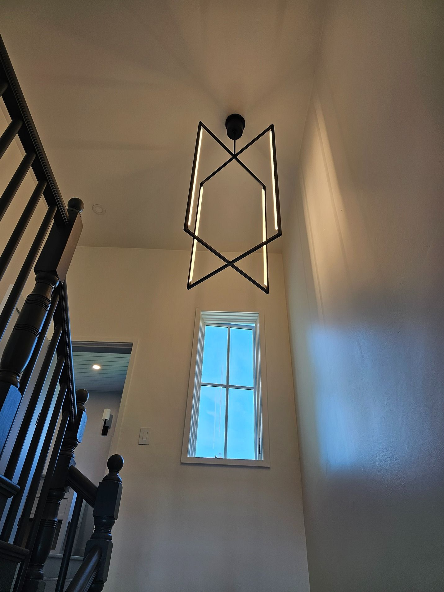 Stairwell with a tall window and a modern black metal light fixture on a cream wall