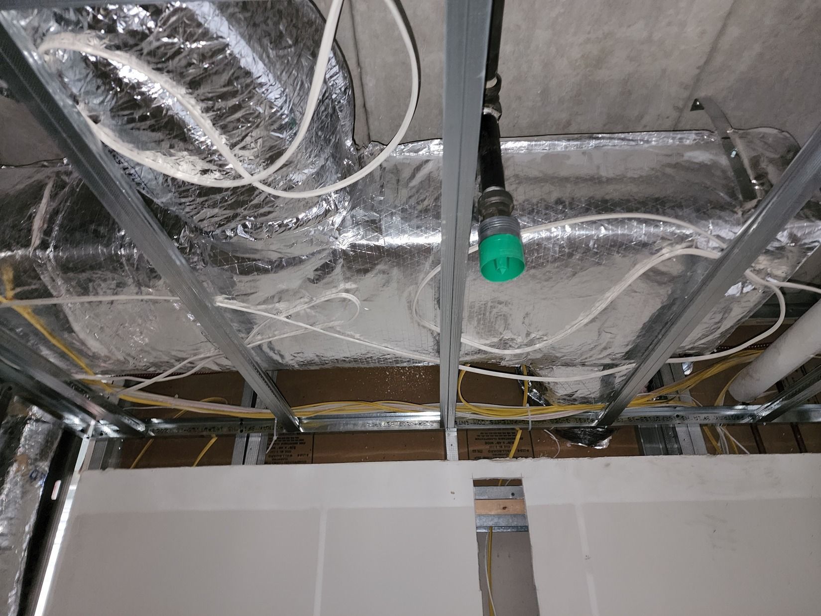 Exposed ceiling ductwork and wiring above a partially installed wall, with a green-capped pipe hanging down