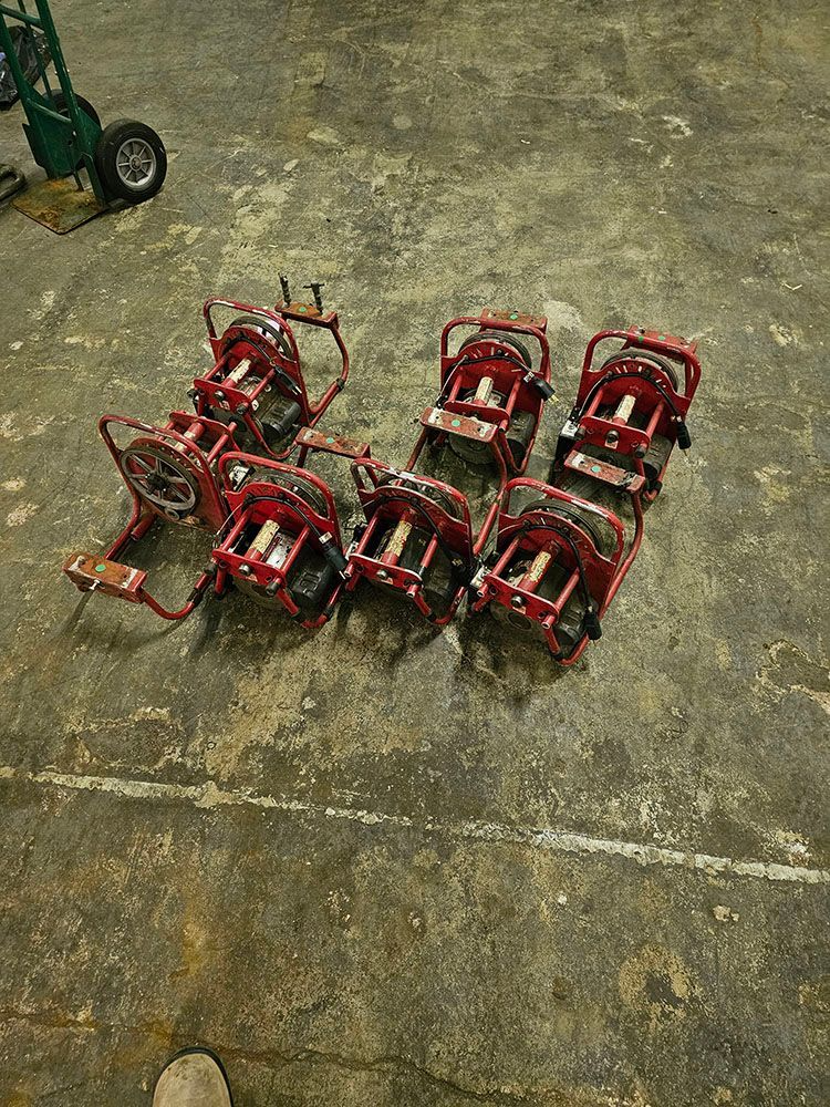 Six red metal frames arranged on a concrete floor, with part of a wheel visible at top left