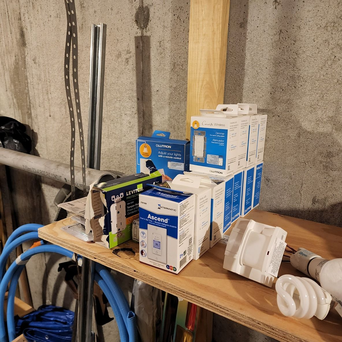 Shelf with stacked blue-and-white boxes, coiled cables, and plumbing parts in a utility room