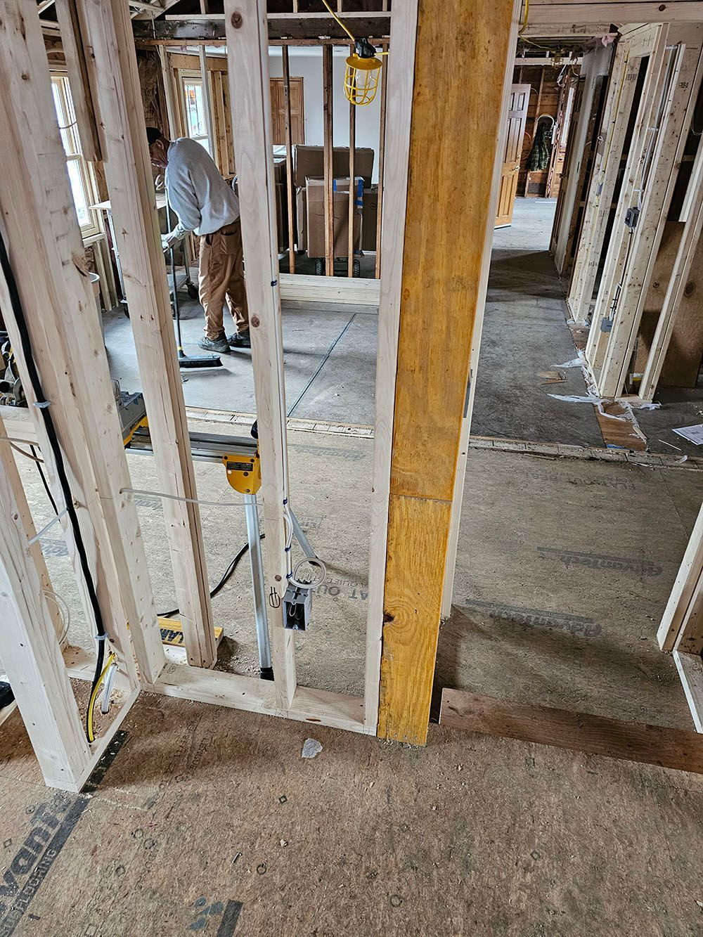 Interior of a construction site with exposed framing and a worker bending over near the back wall.