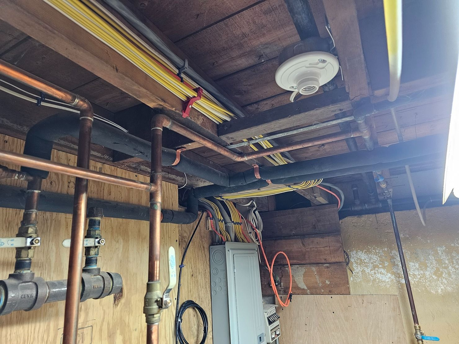 Basement ceiling with exposed pipes, wiring, and a smoke detector near a wooden beam.
