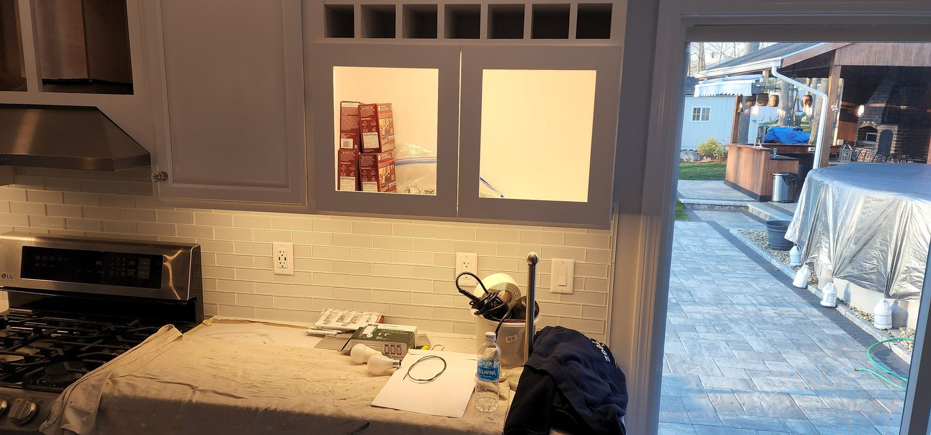 Kitchen with stove and countertop, looking out to a snowy backyard through a bright open door.