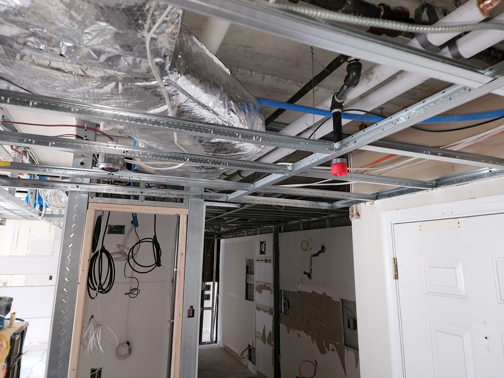 Basement corridor with exposed ceiling wires, open doors, and unfinished walls under renovation