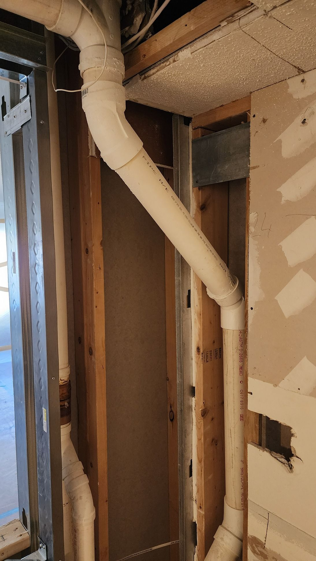 Exposed wall framing with a white vent pipe running diagonally through a partially demolished interior wall