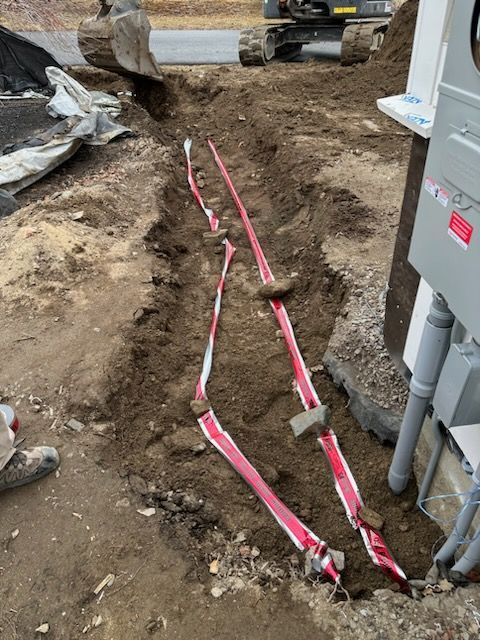 Trenched dirt path with red caution tape beside a house foundation and construction materials