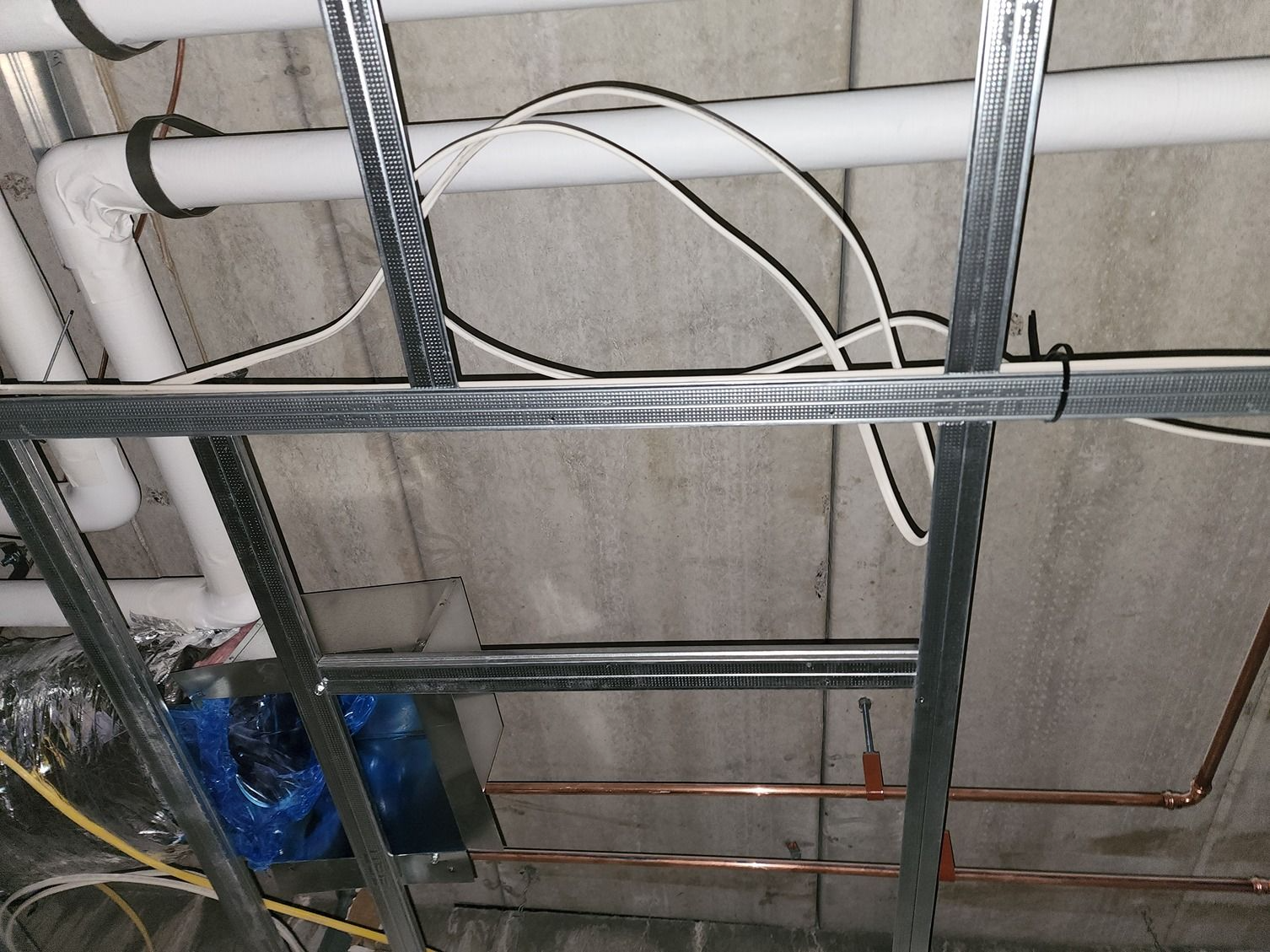 Close-up of exposed ceiling pipes, metal framing, and loose wires in an unfinished interior.