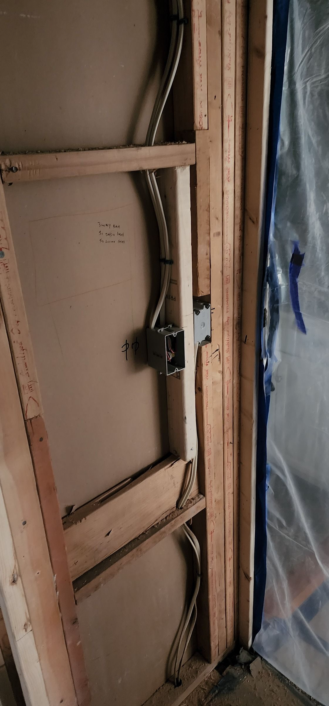 Exposed wooden wall framing with wiring and a translucent plastic sheet on the right side.