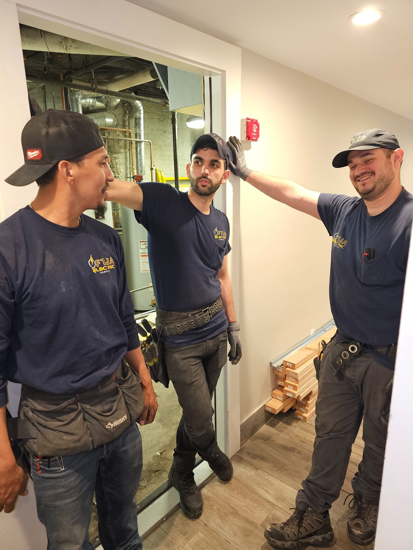 Three workers in navy shirts standing in a hallway beside exposed ceiling work and a window.