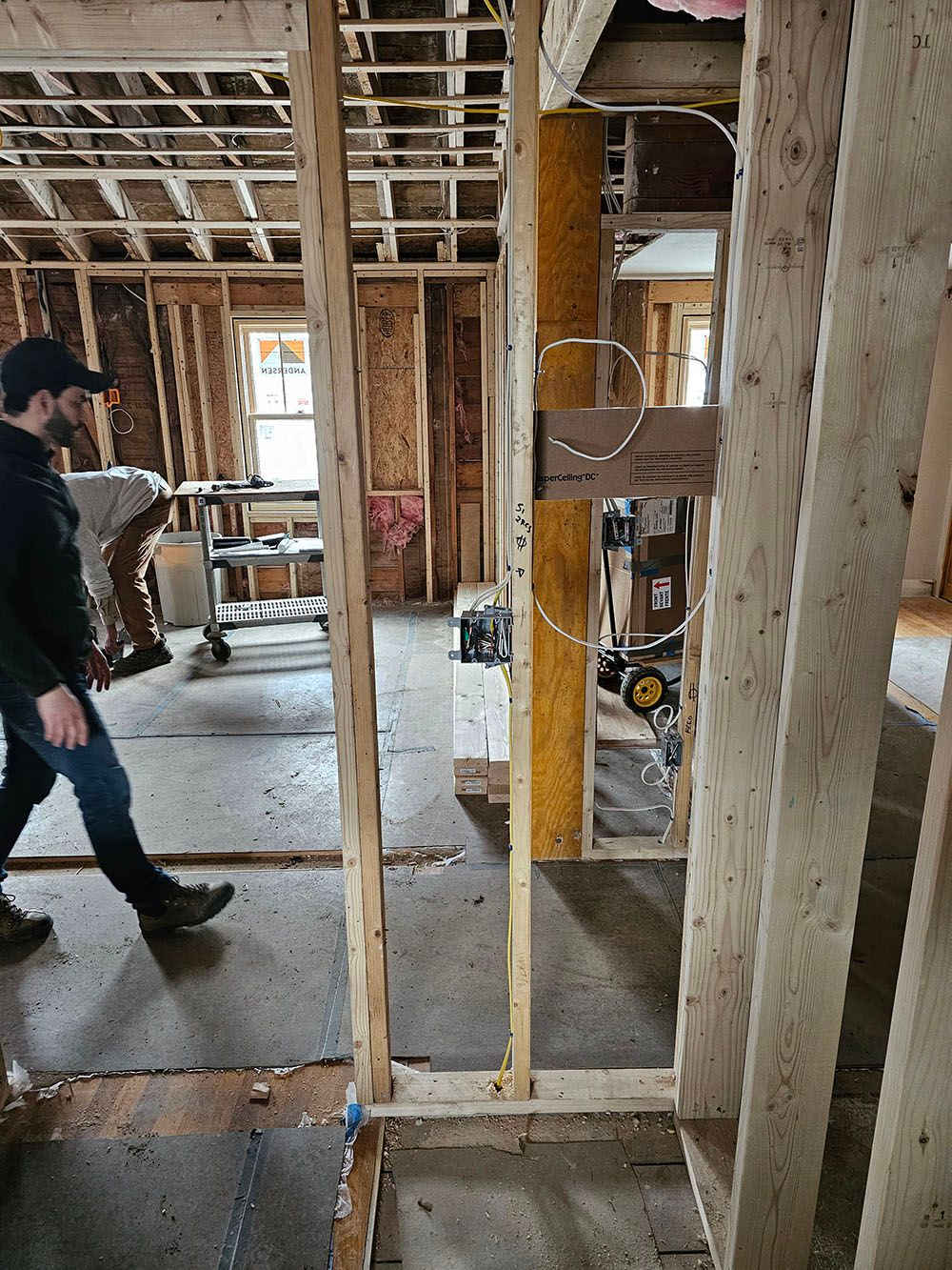 Person walking through a house under construction with exposed framing and unfinished walls