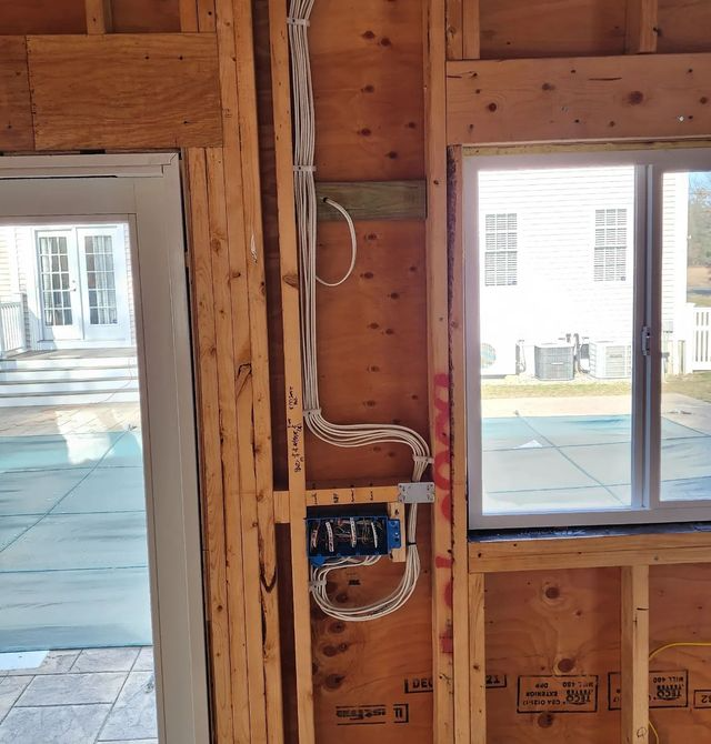 Framed wall under construction with wiring, outlet boxes, and two windows letting in daylight