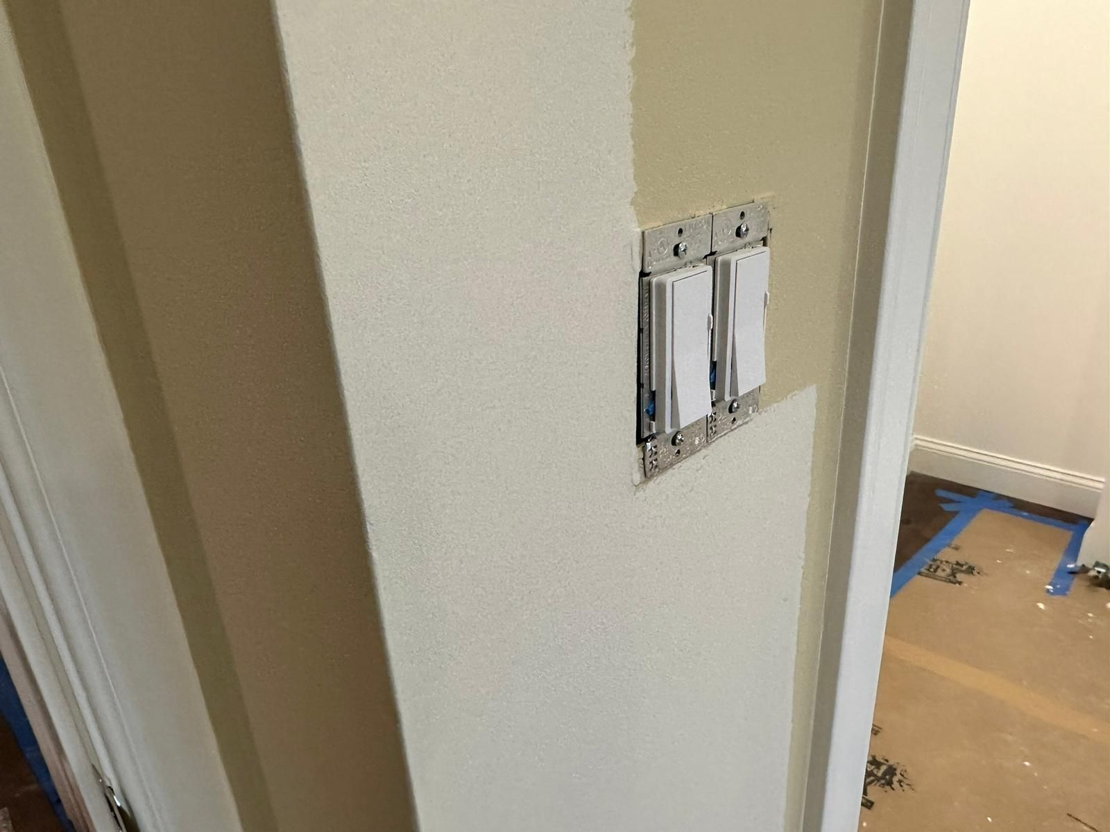 Hallway wall with a light switch panel beside a doorway and a room under renovation beyond it