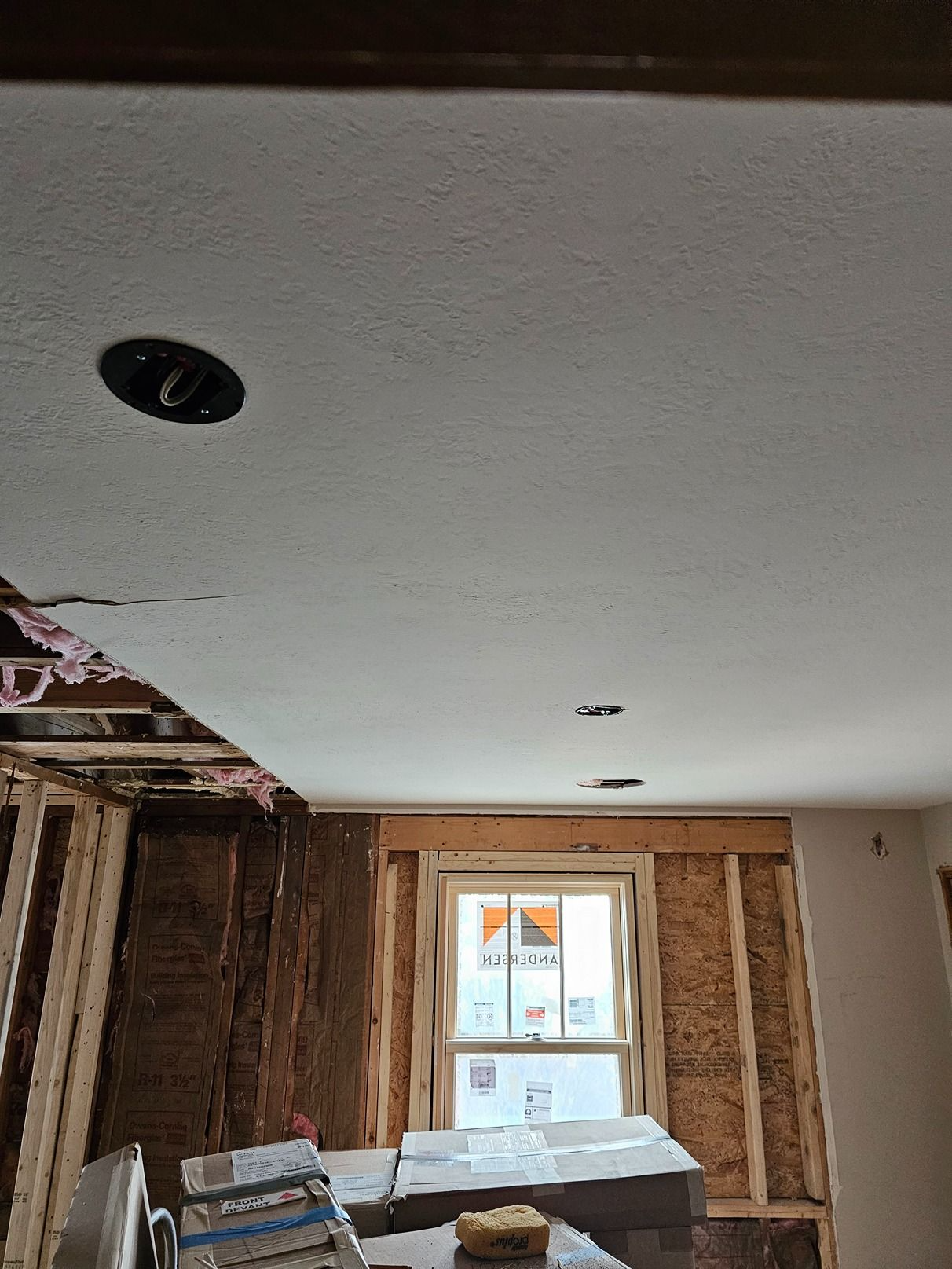Partially renovated room with exposed wall studs, a white ceiling, and a window centered above a workbench.