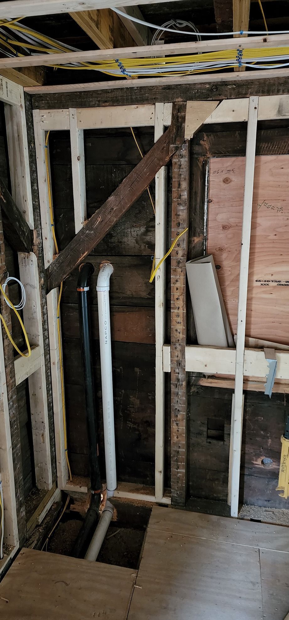 Exposed interior wall framing with a diagonal brace, plumbing pipes, and unfinished flooring in a renovation area