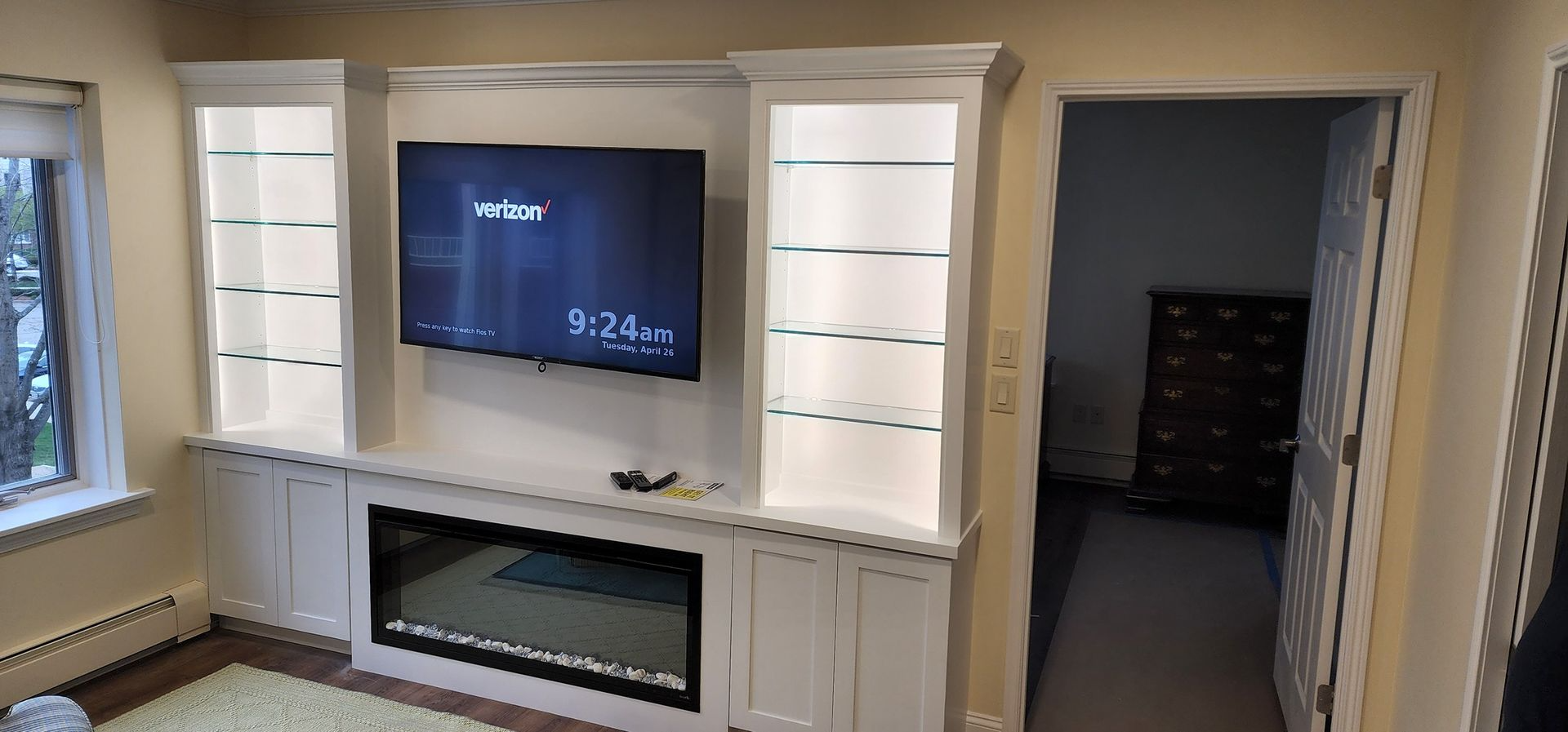 Living room wall with built-in shelves, TV, fireplace, and doorway to a dark room