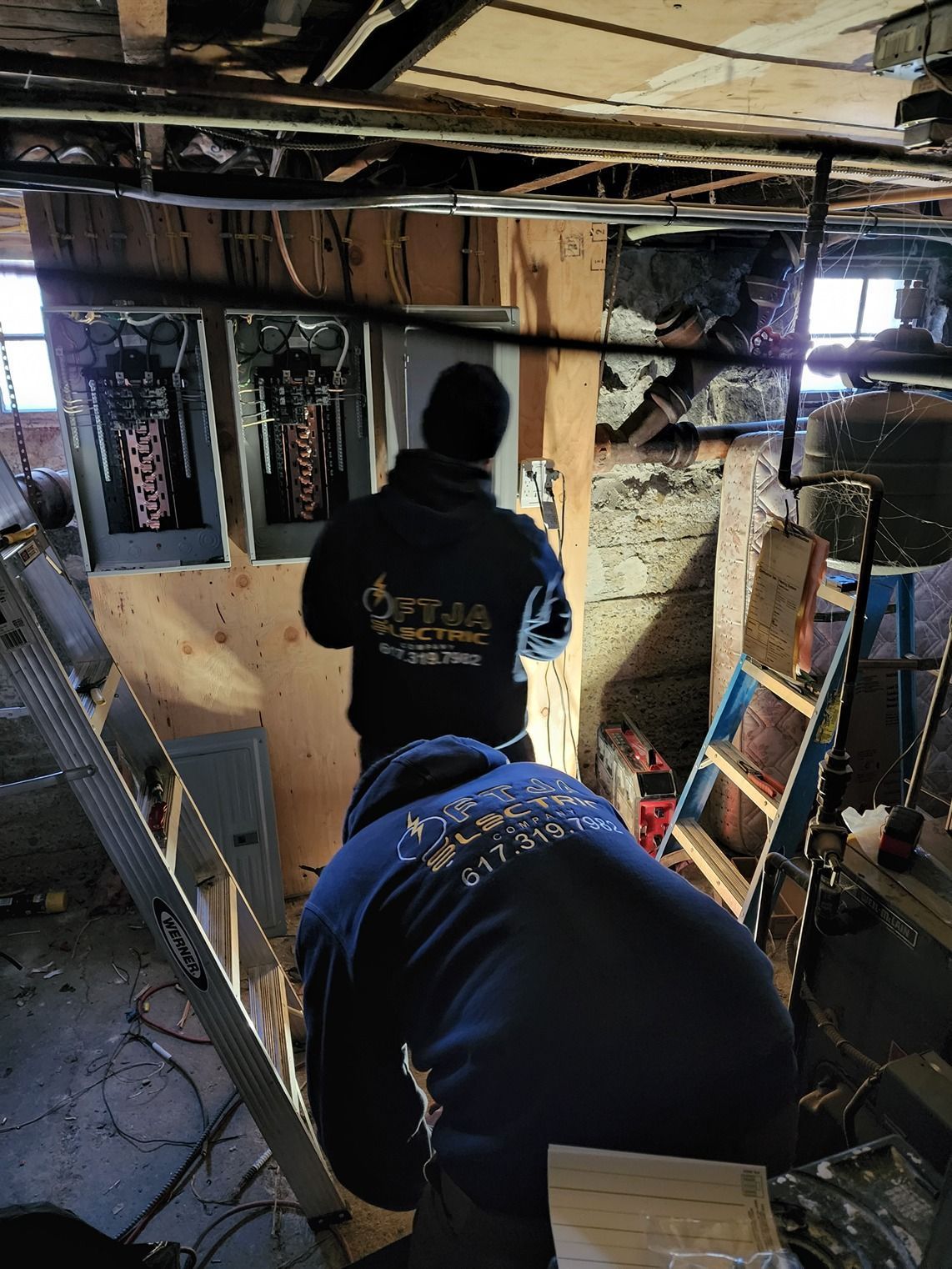 Two workers repair a damaged basement ceiling amid exposed beams and insulation.