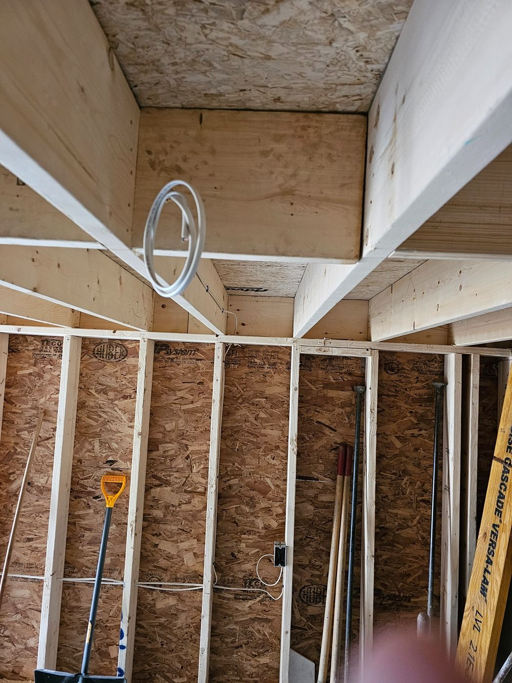 Partially framed room with exposed wood studs, plywood walls, and a looped cable hanging from the ceiling