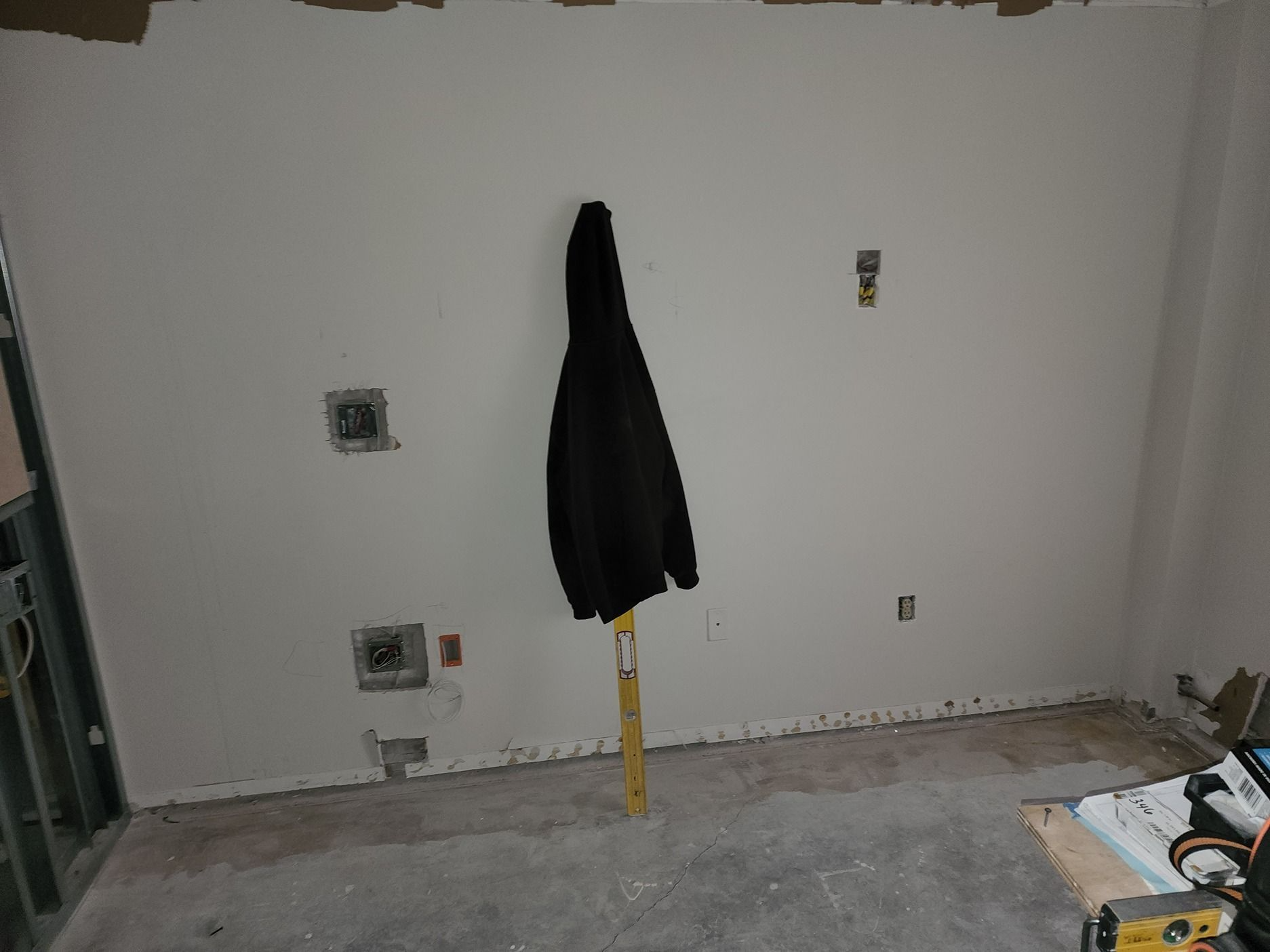 Empty room with white walls, a black coat hanging on a yellow stand, and tools scattered on the floor.