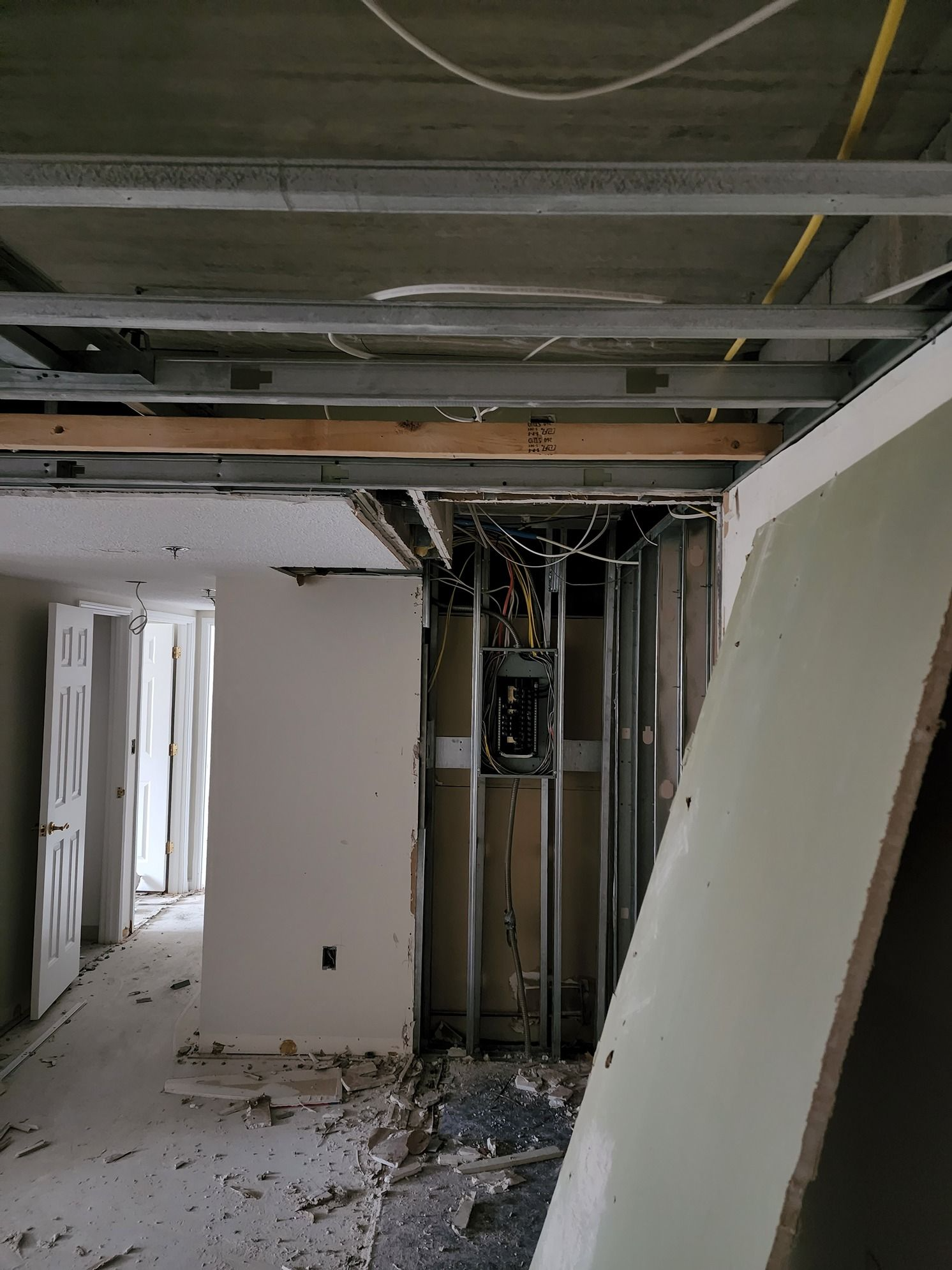 Damaged interior hallway with exposed ceiling beams, broken drywall, and construction debris on the floor