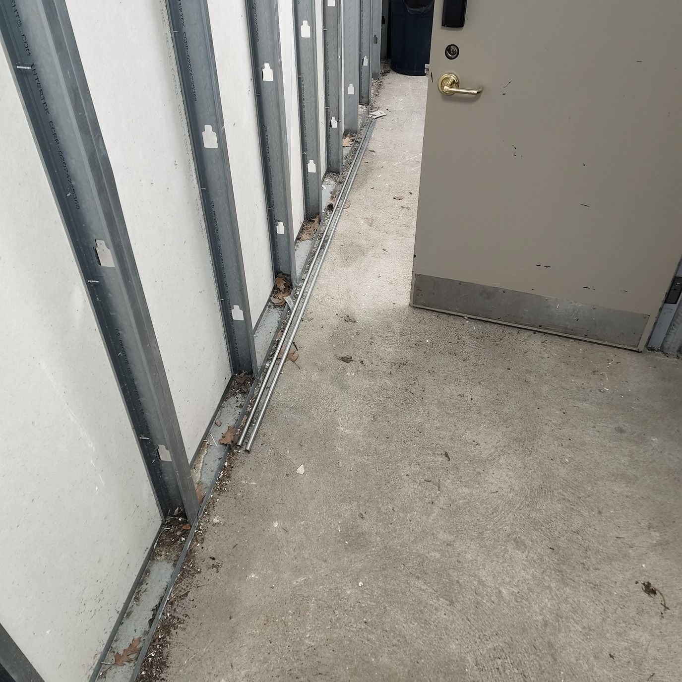 Narrow concrete corridor with gray walls, a door, and debris along the floor edge