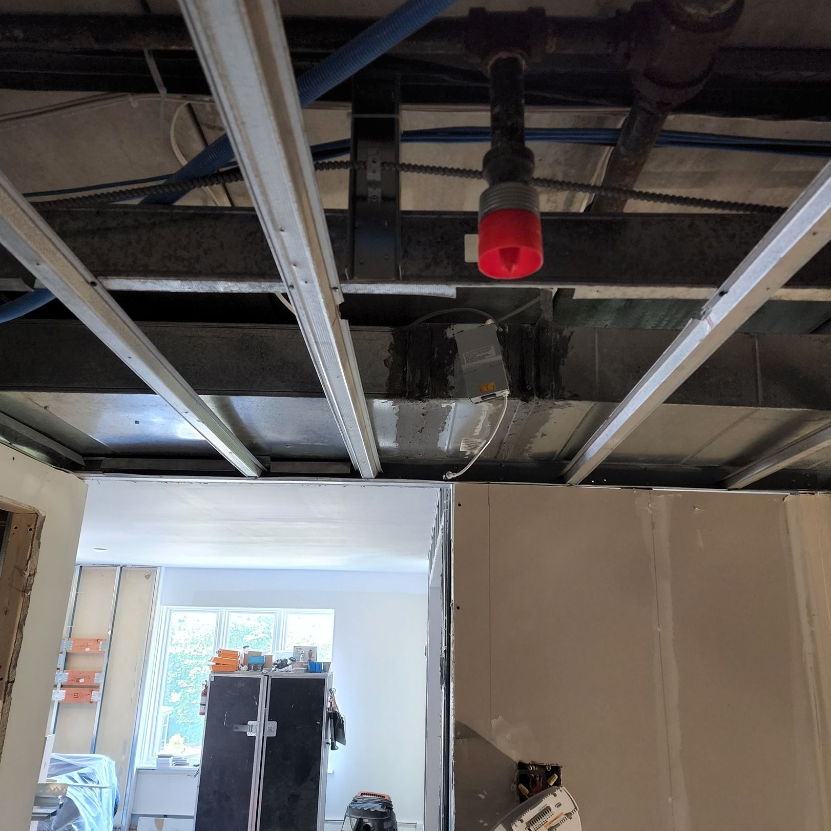 Exposed ceiling framing with red sprinkler cap above a doorway in a partially renovated room