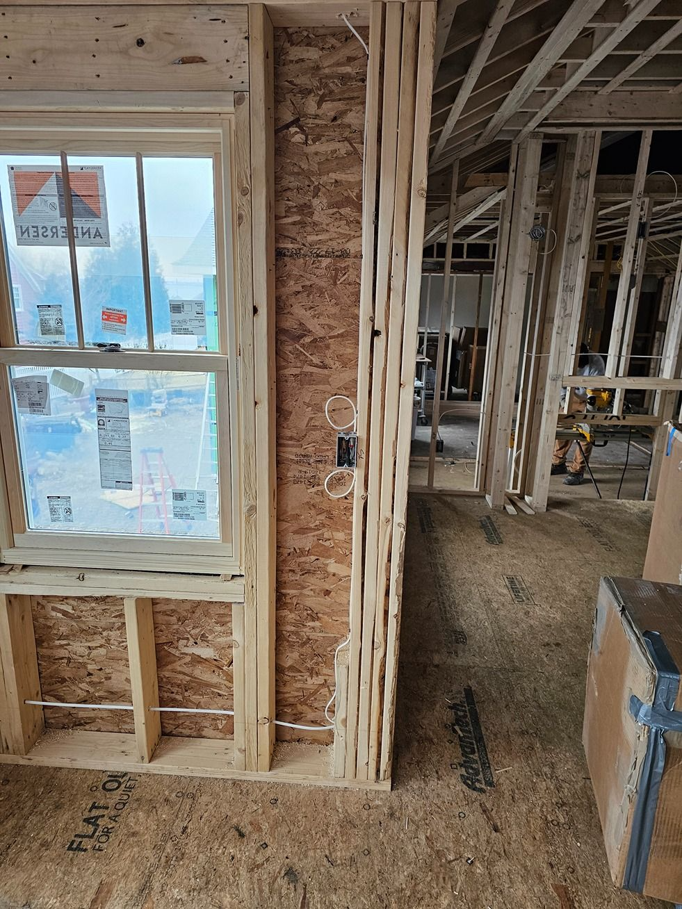 Interior construction site with unfinished wood framing, a window, and exposed wiring.