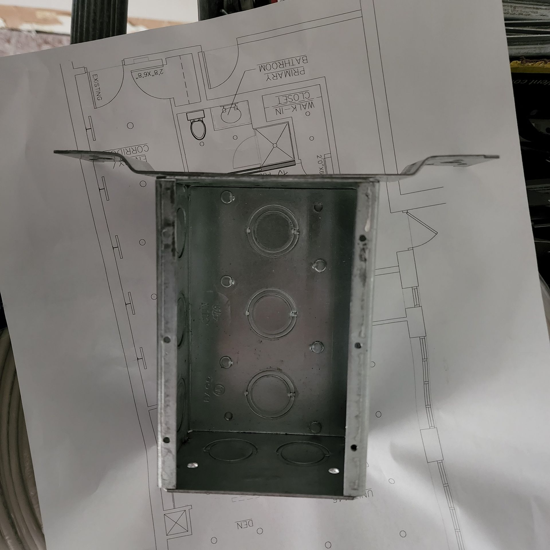 Metal electrical junction box mounted on a wall, centered over a penciled-in construction diagram.